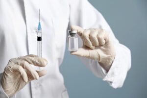 Person in lab coat and gloves holding a syringe and vial of liquid.